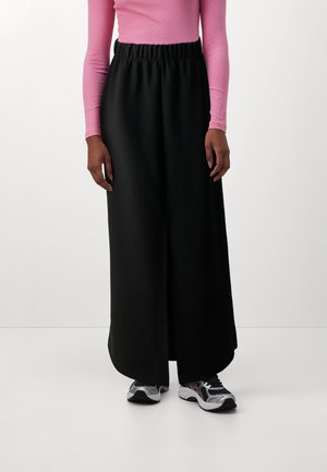 Svart, lang, flowy skjørt med elastisk linning, kombinert med en tettsittende rosa langermet topp og svarte joggesko. Jevnt, pustende stoff.