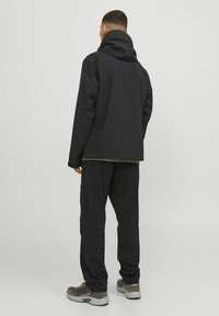 Schwarze Kapuzenjacke, die mit passenden Hosen getragen wird, bietet eine lockere Passform, glattes Material und eine subtile Textur. Graue Sneaker vervollständigen den Look.