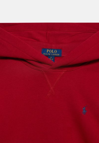 Κοντινό πλάνο μιας κόκκινης μπλούζας Polo Ralph Lauren με κουκούλα που δείχνει την μπλε και κίτρινη ετικέτα της μάρκας μέσα στο γιακά και μικρό μπλε κεντητό λογότυπο στο στήθος.