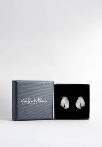 Silberne, strukturierte Ohrstecker, die in einer mit schwarzem Samt ausgekleideten Box mit glänzend schwarzer Außenseite und weißer Markenkennzeichnung präsentiert werden.