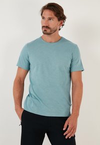 Tricou cu mânecă scurtă și guler rotund, de culoare teal deschis, fabricat dintr-un material moale; textură netedă cu un model subtil heather.