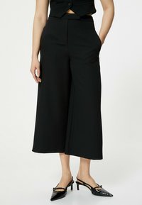 Zwarte wijde broek gemaakt van glad materiaal met een middelhoge taille en zijzakken, gecombineerd met stijlvolle zwarte high heels.