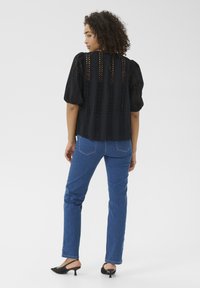 Sort øjelet bluse med puffærmer, parret med blå lige bukser og sorte slingback hæle. Glat stof og mønstrede accenter.