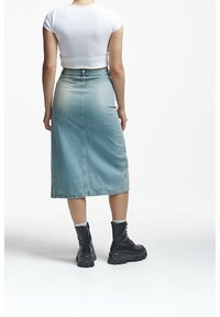Denim midi skirt in light blue with a slight fade, featuring a back slit and a straight silhouette paired with black chunky lace-up boots.