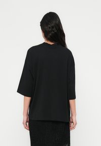 T-shirt preta oversized em tecido macio com mangas curtas, decote arredondado e ajuste relaxado, usada sobre uma saia preta de renda texturizada.