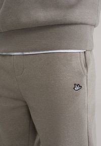 Khakifarvede sweatpants i bomuld med en ribstrikket linning og sidelommer, med et sort broderet logo på venstre lår.