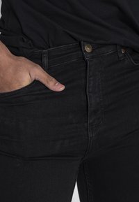 Musta farkkushousu slim fit -mallissa, jossa on etutasku ja kultaiset nappikiinnitykset. Sileä pinta, jossa on vähäiset ompeluyksityiskohdat.