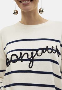 Pullover bianco con strisce orizzontali blu scuro e testo ricamato in nero "bonjour". Presenta un collo rotondo e una texture a maglia morbida.