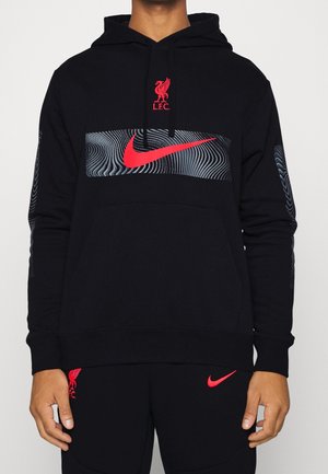 Persoon draagt een zwarte hoodie en broek met rode Liverpool FC- en Nike-logo's, en een golvend grijs patroon achter de grote Nike-swoosh op de borst.