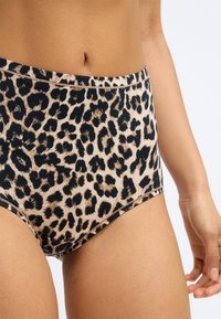 Culotte taille haute au motif léopard, fabriquée dans un tissu doux et extensible avec un fond beige clair et des taches noires.