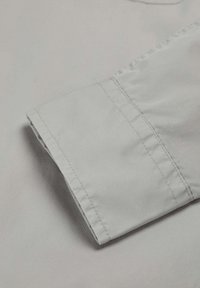 Tejido gris claro con una textura suave, que presenta una manga doblada y detalles de costura limpios. El tejido parece ligero y duradero.