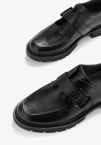 Mustad mustad nahast kingad sujuva viimistlusega, millel on lai rihm pandlaga jala ülemise osa kohal ja paks tekstureeritud kummist tald.