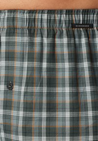 Boxer in tartan nelle tonalità di verde, grigio e arancione. Realizzati in tessuto morbido, presentano un cinturino elastico e un'etichetta nera singola nella parte superiore.