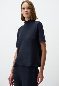 Maglietta blu navy a maniche corte con collo alto e tessuto texturizzato, caratterizzata da una vestibilità comoda e spacco laterale per facilità di movimento.