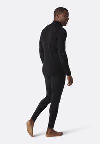 Zwart langemouwen basislaag met een aansluitend ontwerp, contrasterende witte stiksel, rekbare stof en taps toelopende benen voor actieve kleding.