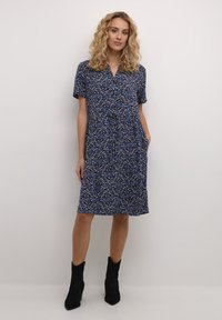 Rochie cu mâneci scurte, până la genunchi, cu imprimeu floral albastru și accente galbene, realizată dintr-un material ușor, cu închidere cu butoane pe față și buzunare laterale.