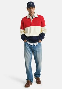 Rood, wit en marineblauwe gestreepte langemouwen polo shirt met een kraag, gecombineerd met lichtblauwe jeans en bruine veterschoenen.