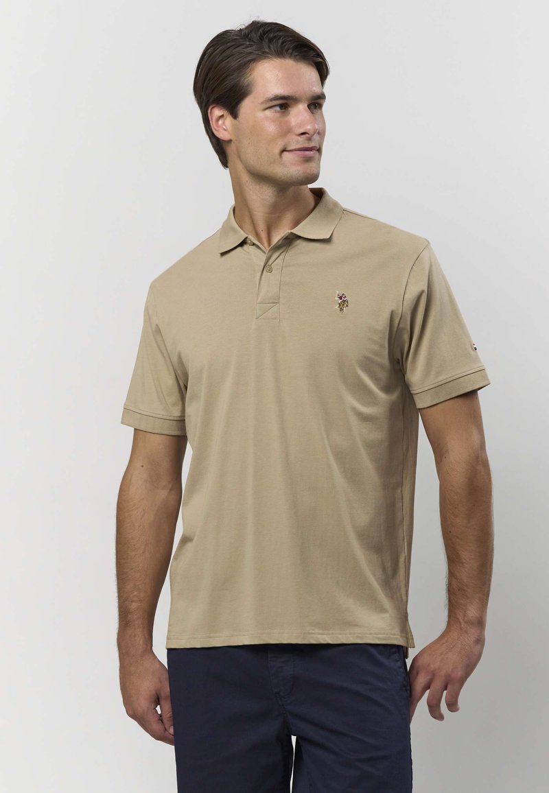 Smelio spalvos polo marškinėliai iš minkštos medžiagos su klasikine apykakle ir trumpomis rankovėmis. Ant kairės krūtinės pusės yra išsiuvinėtas logotipas.