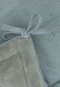 Douce couverture bleue avec un motif en tricot texturé et un doublure en polaire douce, maintenue par un détail de nœud en satin.
