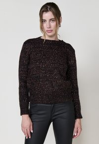 Dunkel gestrickter Pullover mit strukturiertem Muster, weitem Rundhalsausschnitt und langen Ärmeln, kombiniert mit schwarzen, figurbetonten Hosen.
