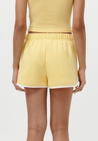 Pantaloni corti di cotone gialli con un elastico in vita, caratterizzati da una rifinitura bianca lungo le aperture delle gambe e una texture semplice e liscia.