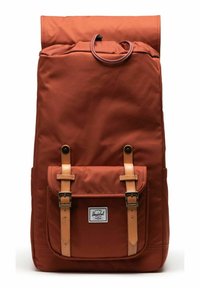 Sac à dos en tissu marron avec un design à rabat, accents en cuir et sangles à boucle. Présente une poche avant et une étiquette de marque très visible.