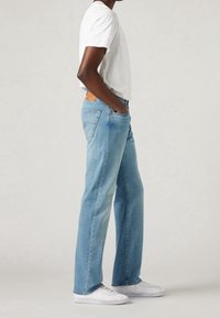 Ljusblå raka jeans i denim, med fem fickor, en brun läderlogotyp på baksidan, i kombination med en vit T-shirt och vita sneakers.