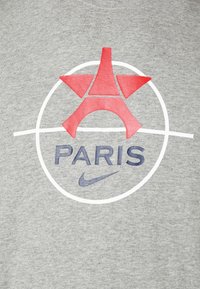 Graues T-Shirt mit einem roten Eiffelturm-Graphic in einem weißen Kreis und dem Wort "PARIS" in Marineblau, sowie einem kleinen Nike-Logo in Marineblau.