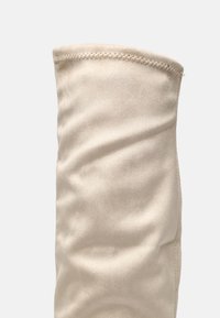 Bota beige por encima de la rodilla hecha de una tela lisa y mate, con una forma ajustada, detalles de costura sutiles y una textura suave.