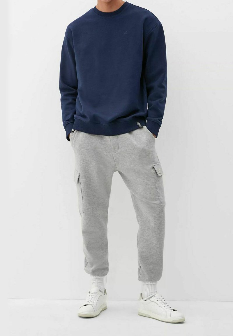 Sweatshirt navy avec des poignets et un ourlet côtelés, associé à un pantalon cargo gris clair avec des poches latérales, complété par des baskets blanches.