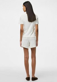 Top corto de manga corta blanco con bordes festoneados, combinado con pantalones cortos a juego. El material parece suave y ligero.