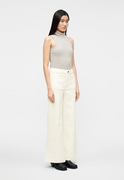 Haut sans manches à col roulé rayé en gris clair et blanc, associé à un pantalon large crème et des bottines noires.