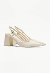 Escarpins à bride arrière en cuir verni beige, présentant un bout pointu, un talon bloc robuste et des sangles de cheville réglables avec un design minimaliste.