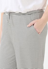 Black and white striped pants with a soft, ribbed texture, featuring an elastic waistband with a drawstring and side pockets.