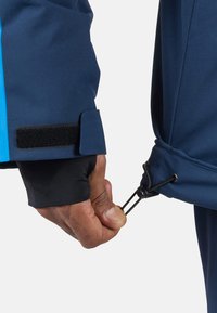 Marineblauer, wasserdichter Jackenbund mit einem schwarzen Klettverschlussstreifen. Hand passt einen elastischen Tunnelzug am Saum an, um einen sicheren Sitz zu gewährleisten.