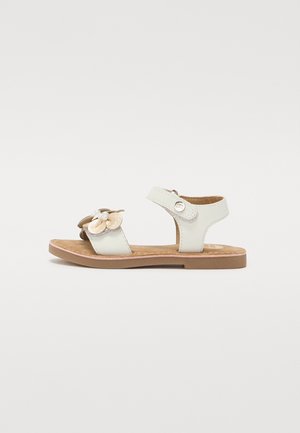 Sandalias infantiles blancas con un diseño de flores, correa ajustable y suela marrón. Hechas de material suave con una plantilla texturizada.