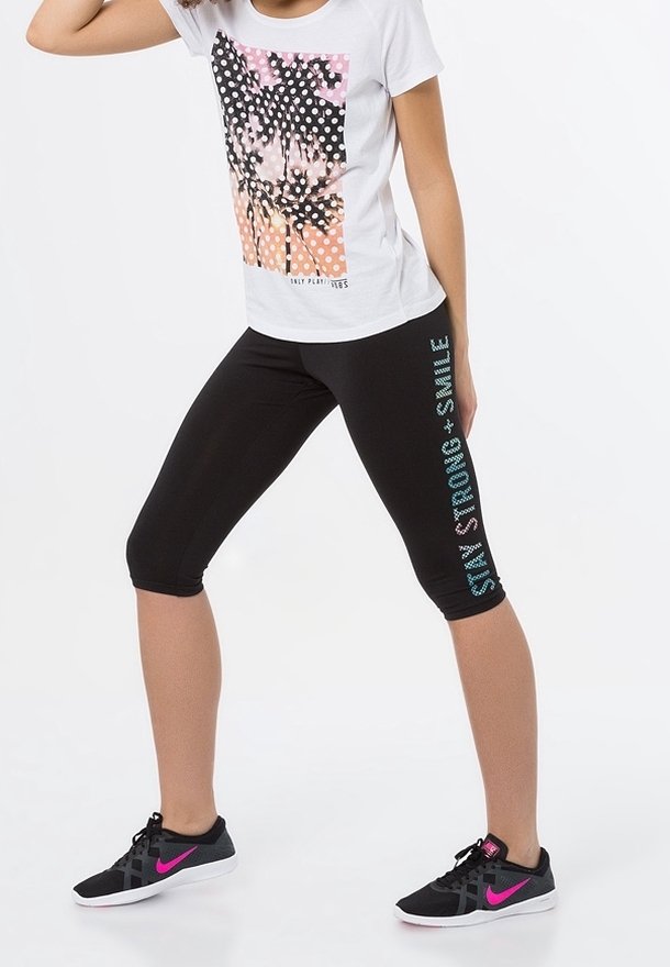 Leggings capri neri con testo 'Stay Strong + Smile' in turchese, abbinati a una maglietta bianca con una grafica colorata di una palma.