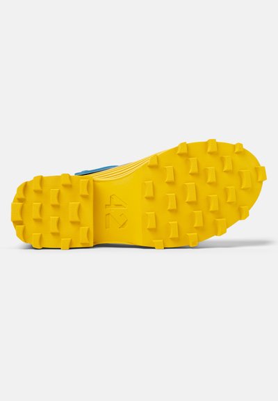 Suola della scarpa con grandi borchie gialle in gomma per una migliore aderenza, superficie testurizzata e design flessibile. Logo del produttore visibile.