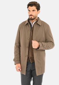 Giacca esterna marrone con colletto, bottoni sul davanti e tasche, abbinata a un cardigan marrone e pantaloni grigi. Texture liscia.