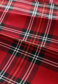 Rød tartan stof med sorte, hvide og gule krydsende striber, der skaber et klassisk ternet mønster med synlig tekstur og folder.