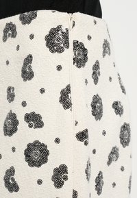 Barna virágmintás, rojtokkal és oldalsó cipzárral díszített krémszínű texturált anyag.