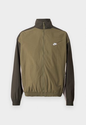 Jachetă Nike de culoare olive, cu guler înalt, mâneci negre în contrast, talie elastică și logo alb pe piept. Material neted, ușor.
