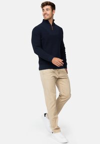 Suéter de punto azul marino con cuello alto y cremallera de cuarto, combinado con chinos beige y zapatillas blancas, con un corte relajado y tejido texturizado.