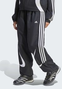 Crne sportske hlače s bijelim prugama, laganog kroja i sjajne teksture. Sadrže Adidas logo i bočne džepove.