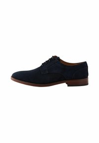 Zapato de vestir de ante azul marino con un acabado suave, punta redonda, seis ojetes para los cordones y una suela marrón en contraste.
