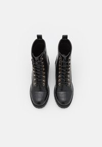 Pár černých kožených šněrovacích bot s krokodýlím vzorem a zlatými oky, z pohledu shora na bílém pozadí.