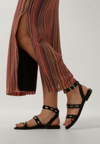 Zwarte leren sandalen met verstelbare banden en zilveren hardware, gecombineerd met een kleurrijke, gestreepte lange rok met een zijsplit.