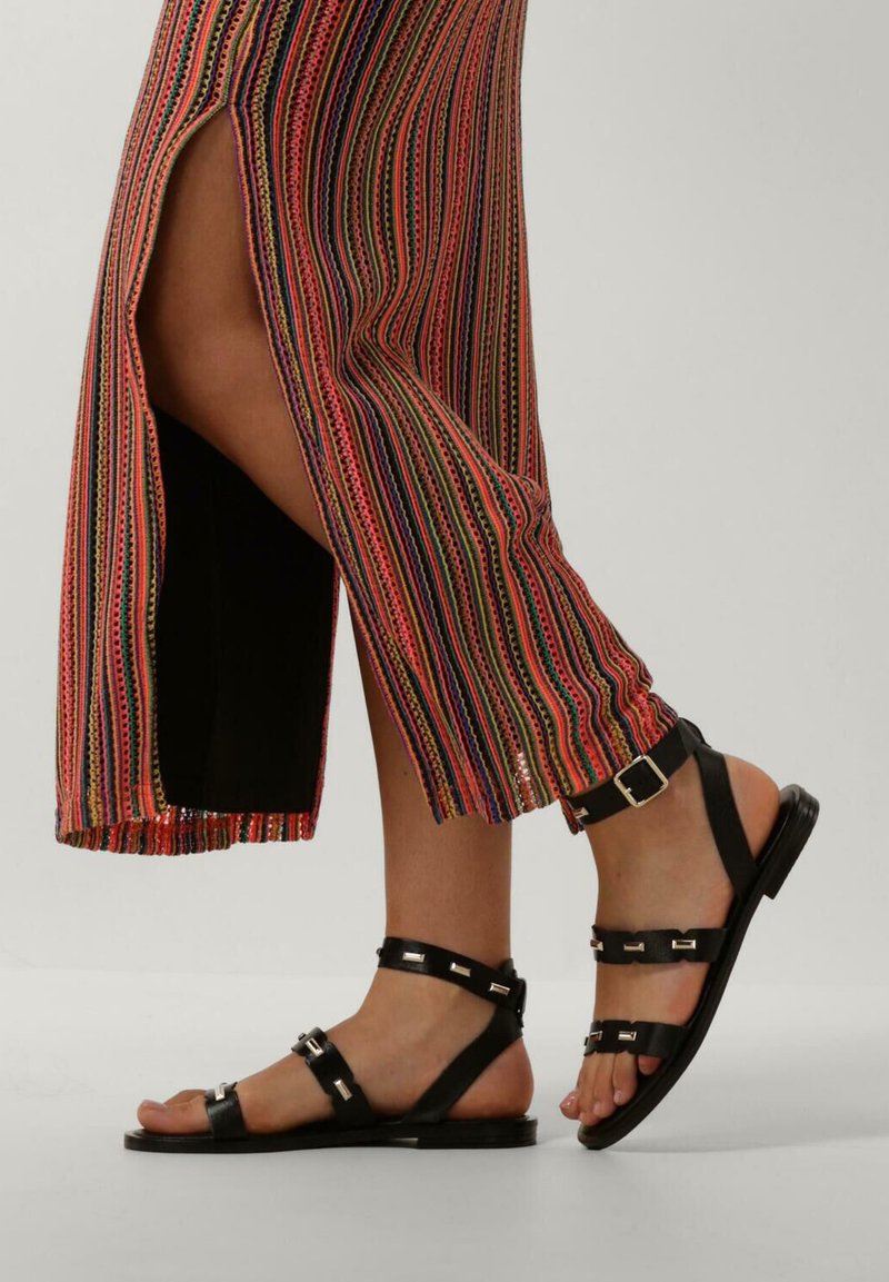 Zwarte leren sandalen met verstelbare banden en zilveren hardware, gecombineerd met een kleurrijke, gestreepte lange rok met een zijsplit.