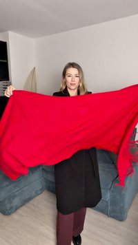 Pătură roșie din lână cu margini franjurate, ținută pentru a arăta dimensiunea și textura. Material neted cu o culoare solidă, evidențiind nuanța vibrantă.