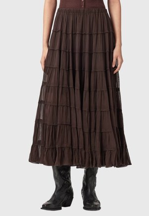 Brun lagdelt maxinederdel kombineret med sorte cowboystøvler, båret af en person stående mod en ensfarvet baggrund.